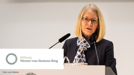 Foto von Cornelia Denz am Rednerpult zur Verleihung des 40. und 41. Werner-von-Siemens-Rings 2022. Links unten die Wort- und Bildmarke der Stiftung Werner-von-Siemens-Ring