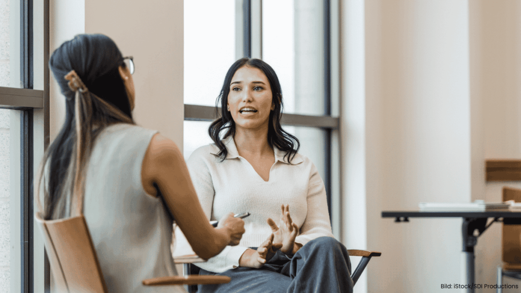 Foto zweier Frauen, die sich auf Stühlen gegenübersitzen unterhalten.
Bild: iStock/SDI Productions